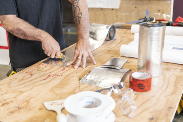 Image of a person cutting a foil membrane with a utility knife on a wooden table with various air barrier tapes