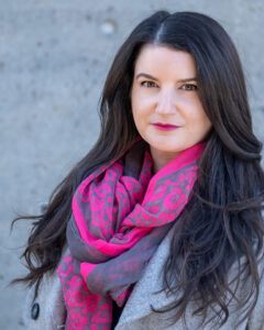 Laura Vail with red lipstick, long black hair, and a pink scarf.