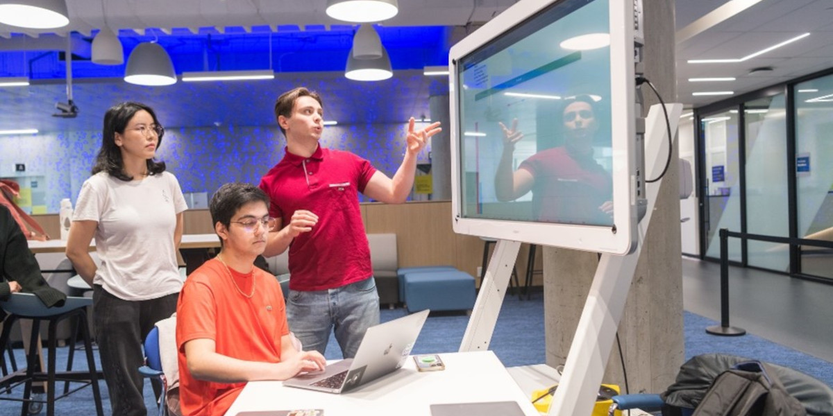 Three students collaborating and looking at a large screen.