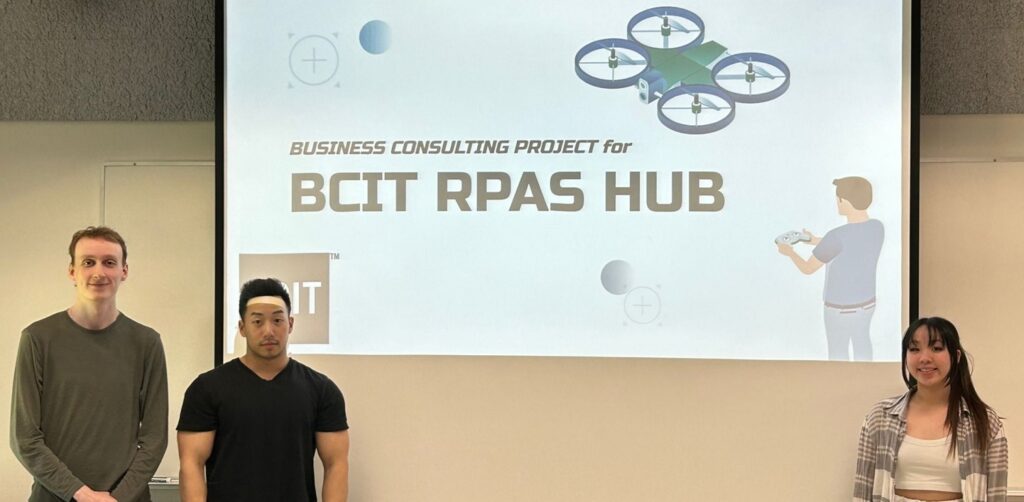 Three people standing in front of a screen that reads "Business Consulting Project for BCIT RPAS Hub"