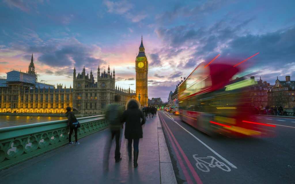 London, England - Iconic Red Double Decker Bus on the move on Westminster Bridge with Big Ben and Houses of Parliament at background. Sunset with beautiful colourful sky.