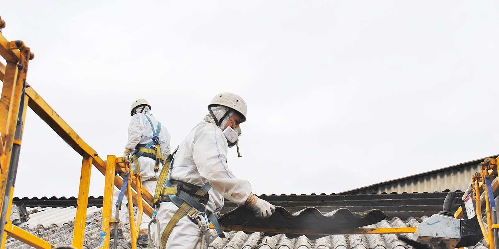 image of 2 workers on roof in white protective gear removing asbestos