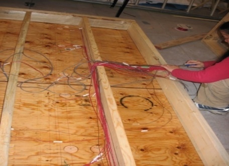 Wood-frame wall test panel lying on floor with sensor cables attached