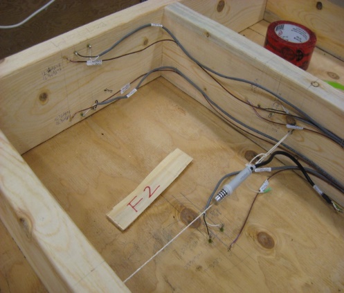 Wood-frame test panel lying on floor with sensor cables attached