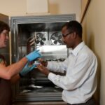 Two men standing in from of an open environmental chamber