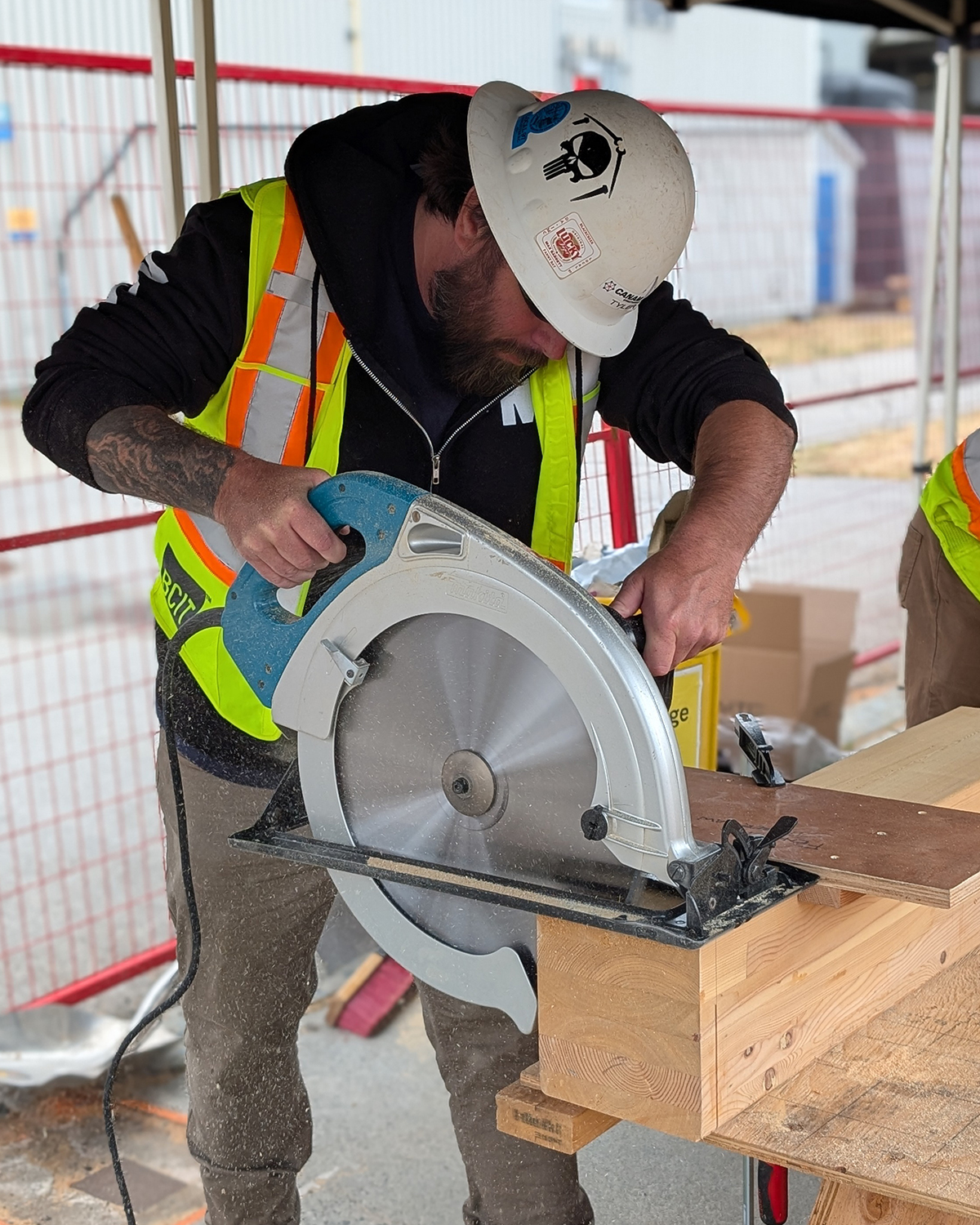 A student wearing a BCIT high-visibility vest uses a circular saw to cut a mass timber component on the practicum site.