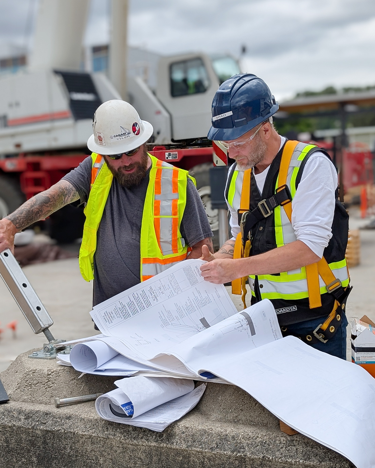 Two BCIT MaTT Hub participants in hard hats and high-visibility vests review structural drawings together on a practicum site.
