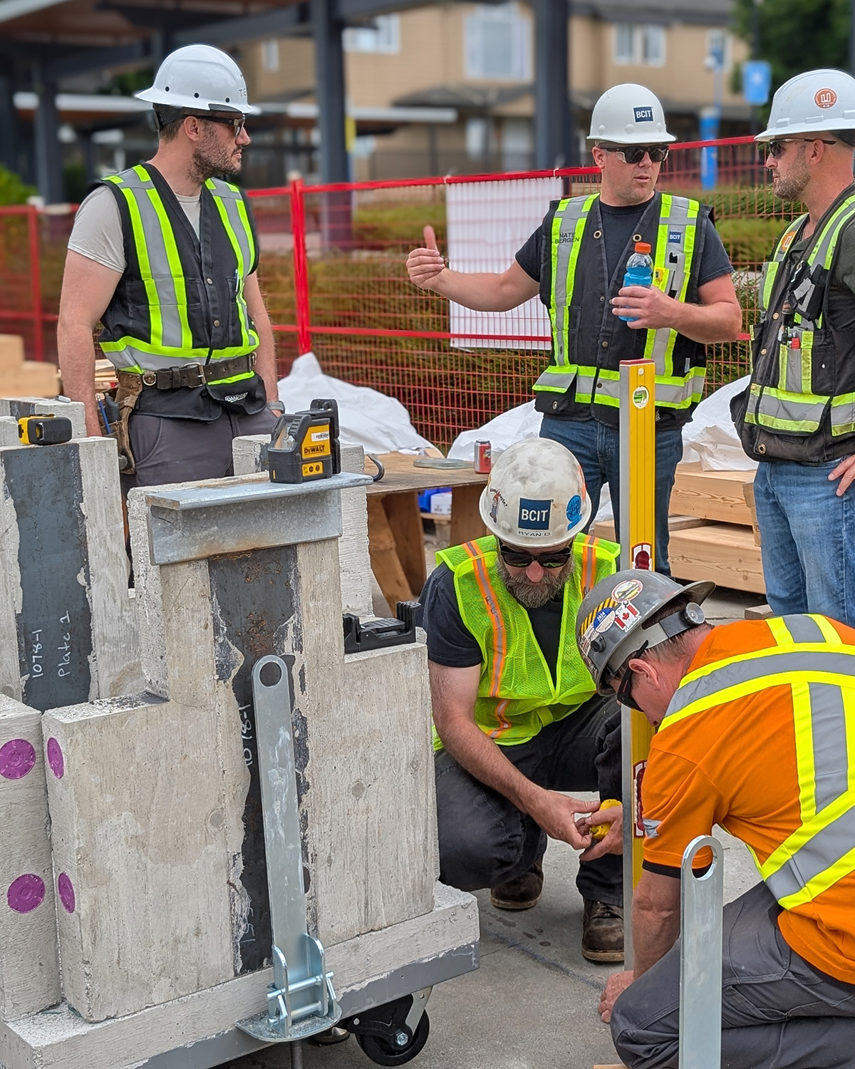 A BCIT instructor briefs four students around a concrete column base plate assembly, demonstrating structural connection tolerances during the practicum.