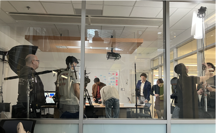 A team of students perform different roles in a video production - holding lights and microphones, organizing actors, setting up video equipment.