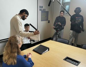 A group of students record a scene in a conference room for a video project.
