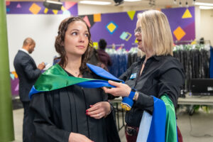 Cynthia helping a student put on their graduation gown.