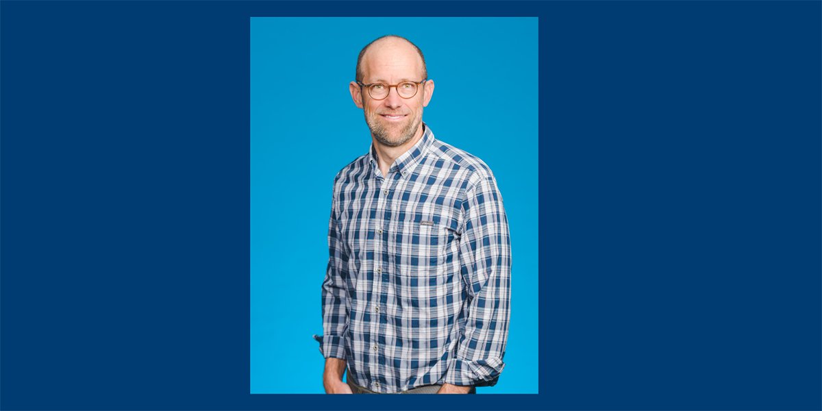 Dr. Eric Anderson standing with a light blue background.