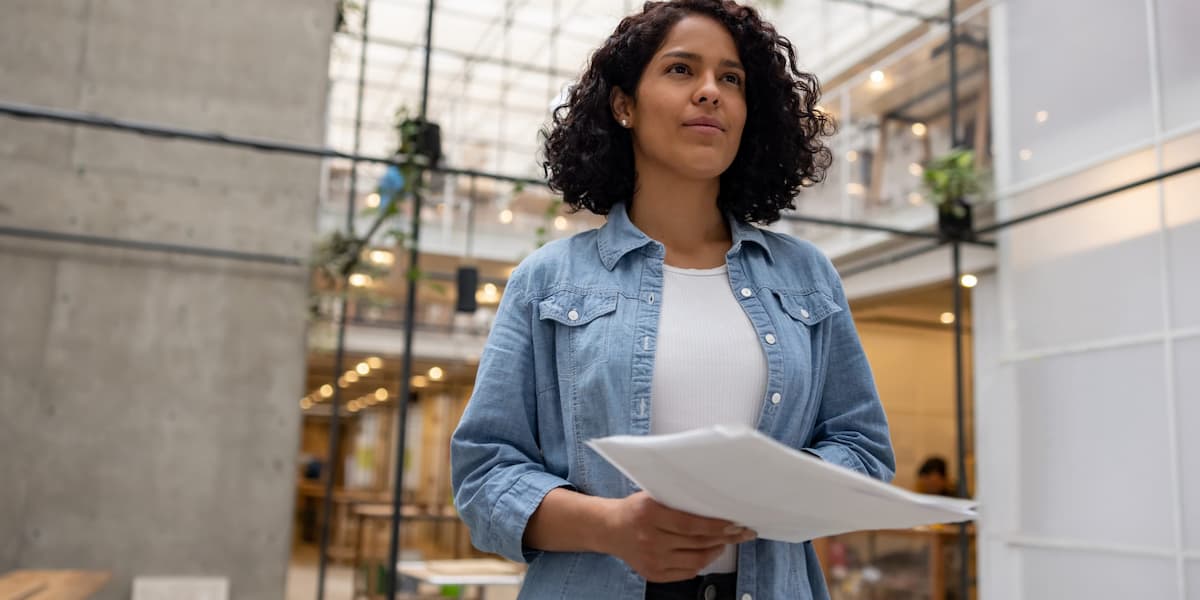 A female-presenting individual holding pieces of paper and looking forward.