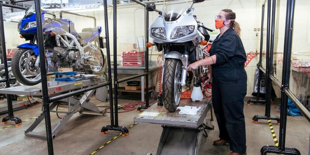 A Motorcycle Technician Foundation student tunes up a motorbike on a hoist in the BCIT mechanic shop.
