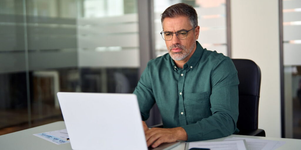Middle aged professional business man investor using computer working at desk.