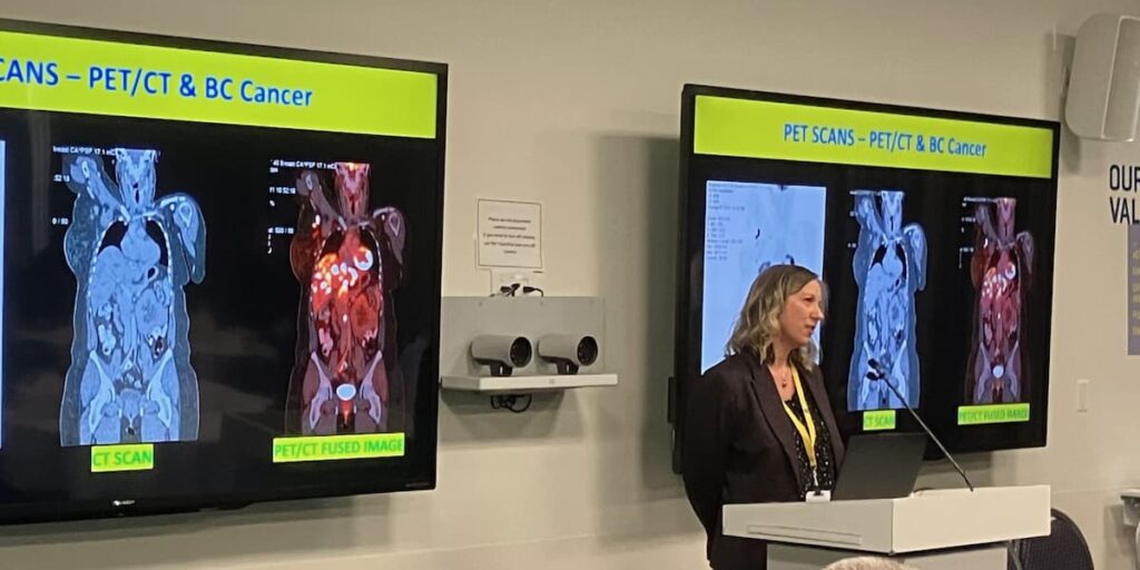 female presenter stands in front of a screen that shows medical scans with the title