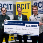 Three people standing in from of three BCIT banners holding a novelty cheque