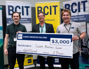 Three people standing in from of three BCIT banners holding a novelty cheque