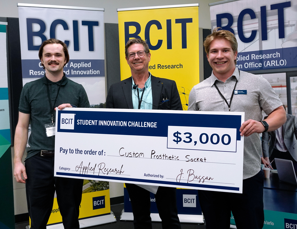 Three people standing in from of three BCIT banners holding a novelty cheque