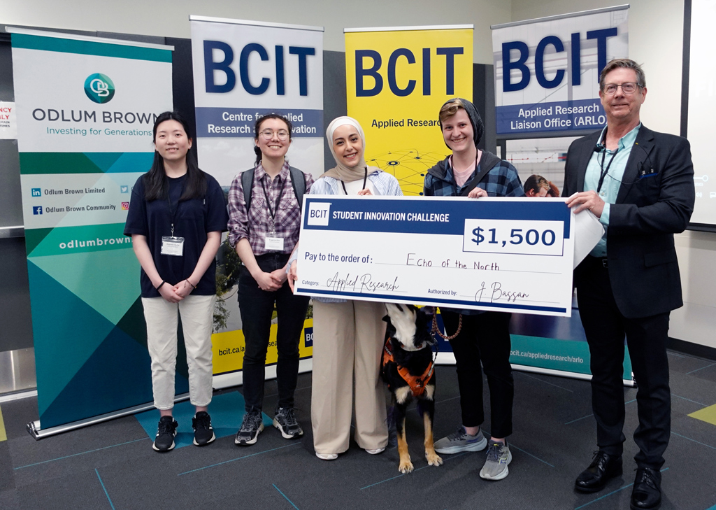 Five people standing in from of three BCIT banners holding a novelty cheque