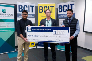 Three people standing in from of three BCIT banners holding a novelty cheque