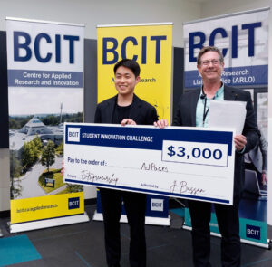 Two people standing in from of three BCIT banners holding a novelty cheque