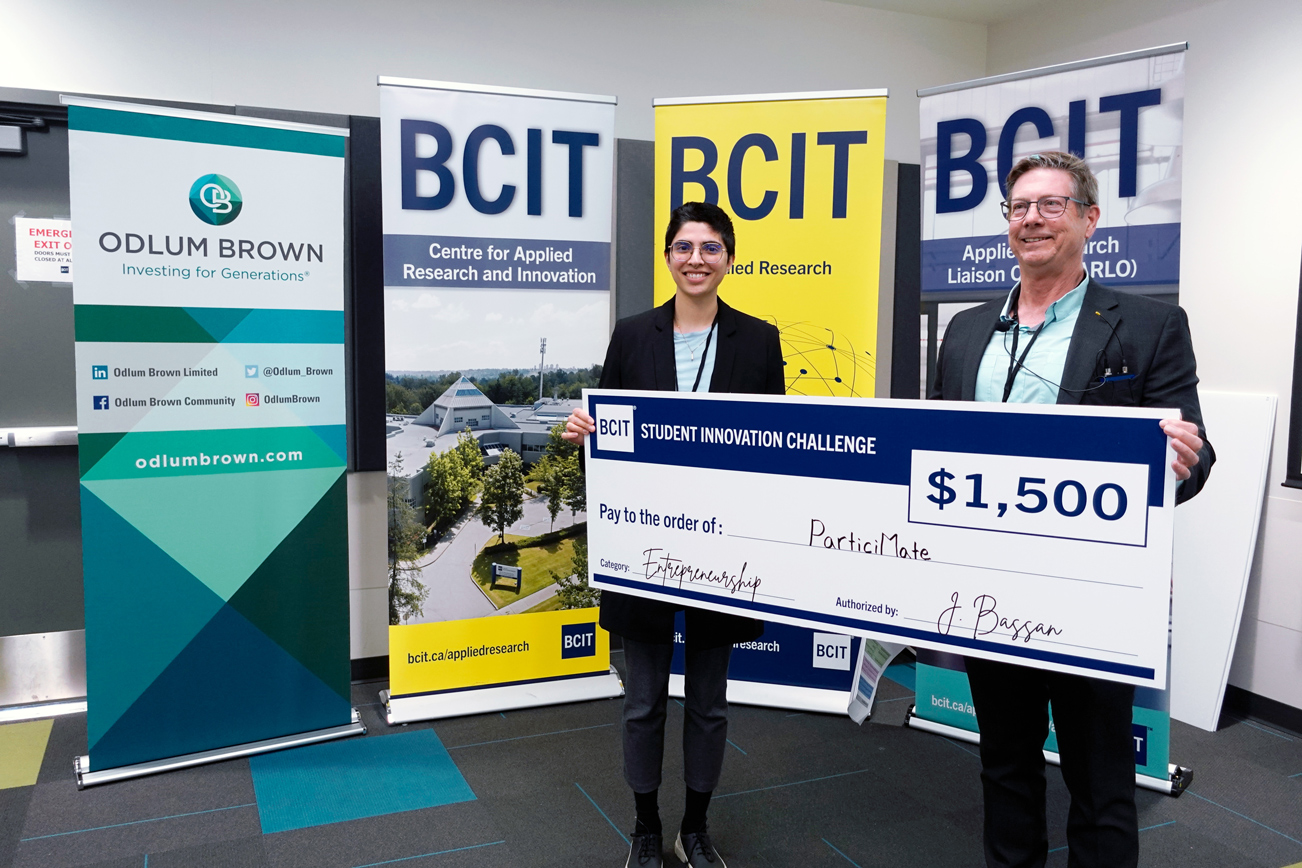 Two people standing in from of three BCIT banners holding a novelty cheque