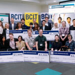 A group of over 30 people grouped in fron of three BCIT banners holding large novelty cheques