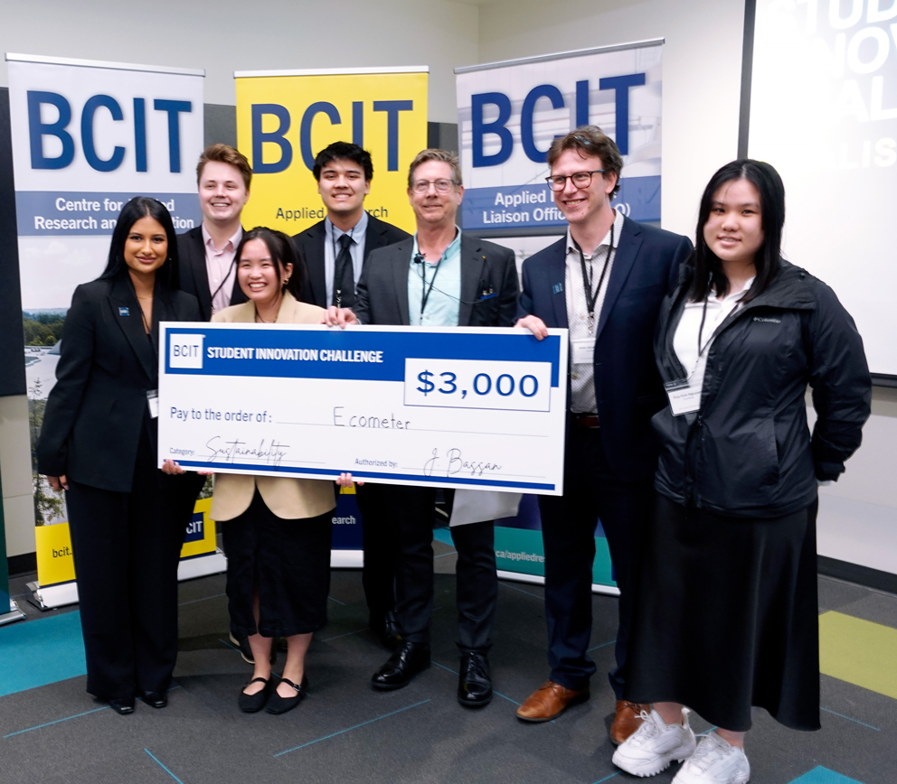 Seven people standing in from of three BCIT banners holding a novelty cheque