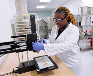 woman in lab coat standing by a 3d food printer
