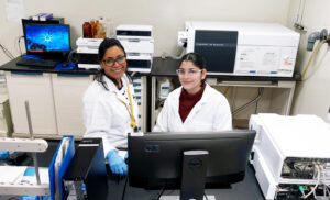 Two women in lab coats in front of a computer screen