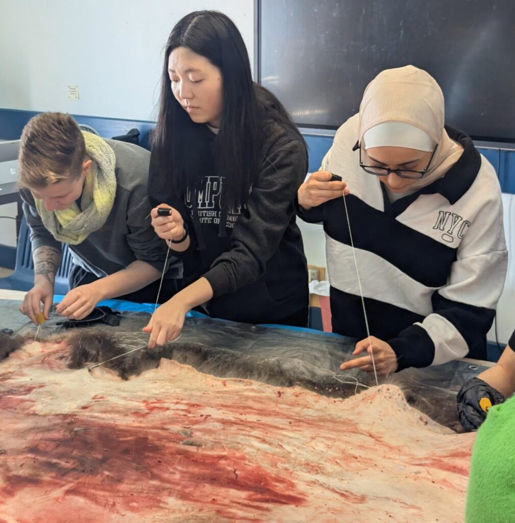 three women sew an animal skin