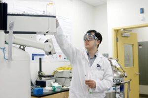 man in labcoat and safetyy glasses working in a lab