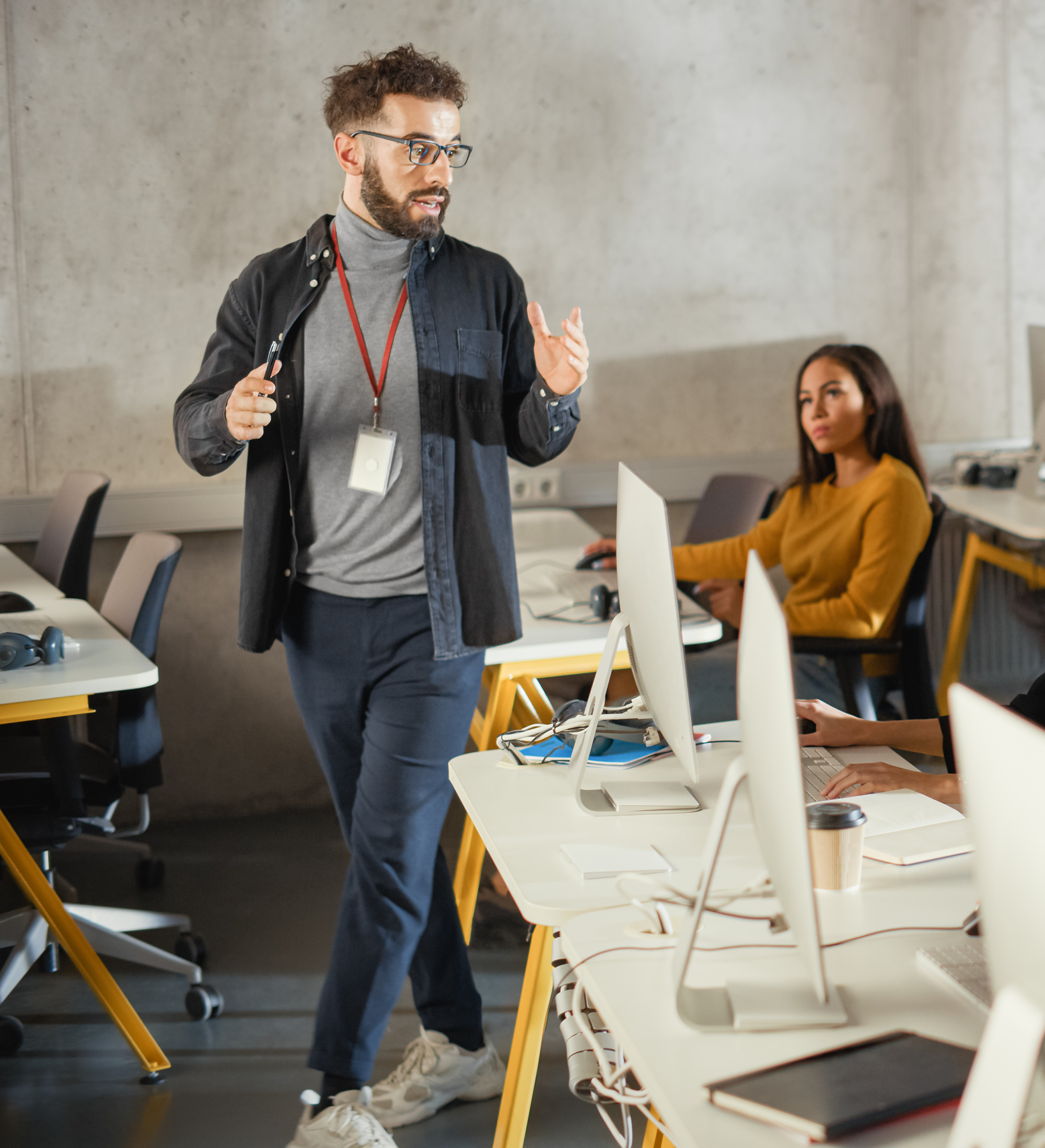 instructor speaking expressively to a group of students seated in front of monitors