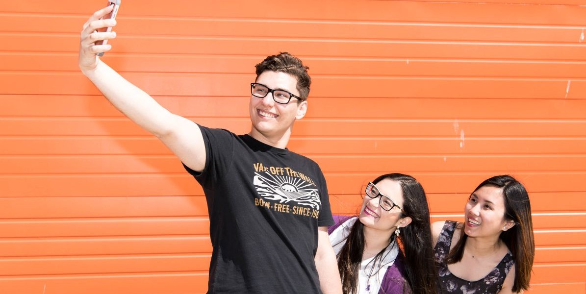 three smiling young adults posing for selfie photo