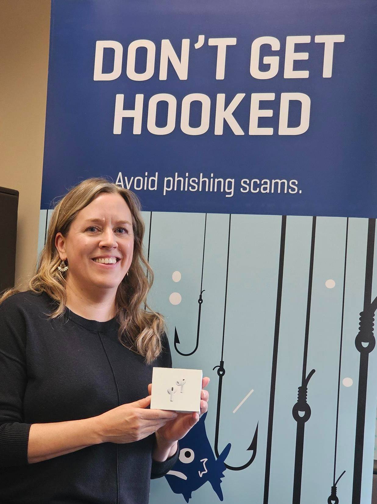 2025 winner of Cybersecurity Awareness Month holding Apple AirPods prize in front of banner reading "Don’t get hooked. Avoid phishing scams."