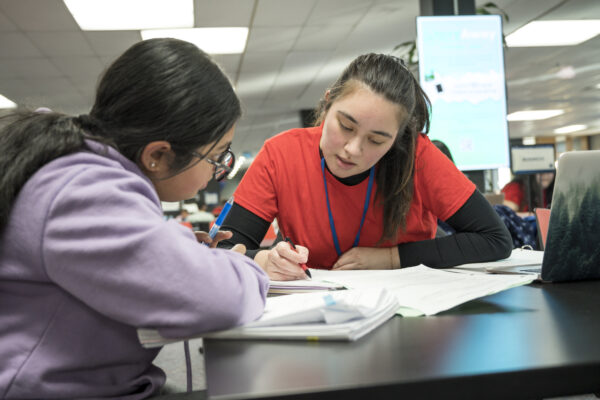 A peer tutor in a red shirt works with a student