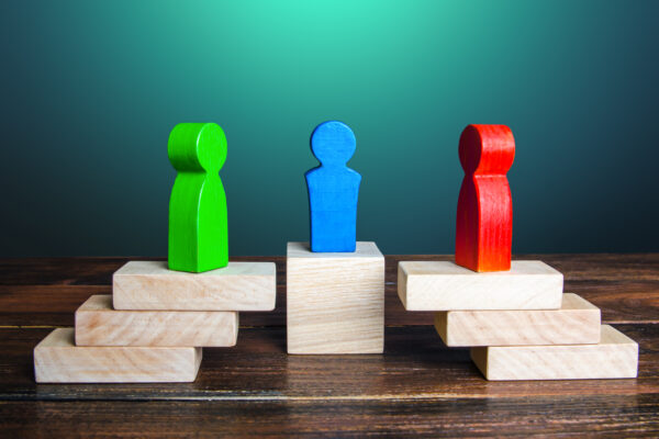 Three wooden people-shaped objects are each on three blocks, with a green and red one facing opposite of each other and a blue one is in between them.