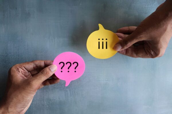 Two hands on opposite dies holding chat bubble post-it lots, one with a question mark and the other an exclamation mark, indicating a conflict between the two people.