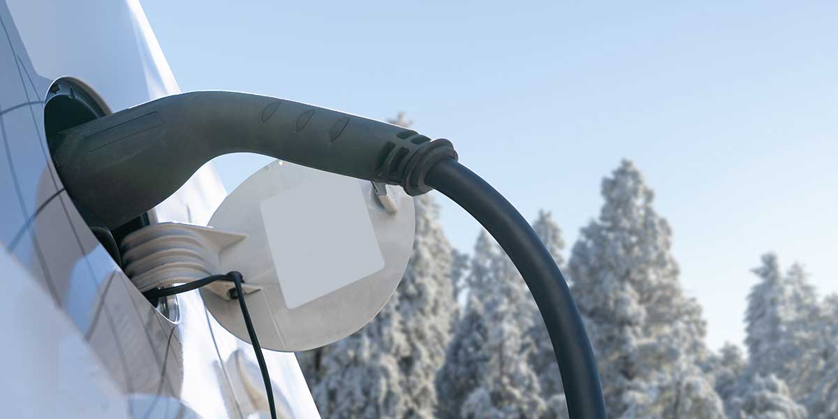 close up of an ev charger plug plugged into a vehicle against a winter sky background