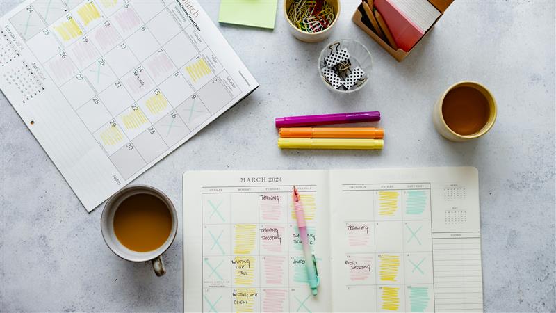 A colour coded planner on a table with coffee cups and highlighters.