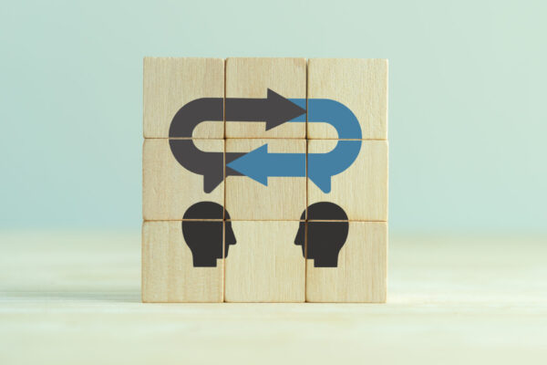 Six wooden blocks stacked with an image of two people facing each other and a chat bubble on top with circular arrows indicating dialogue and feedback.