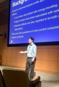 man presenting at the front of a theater in front of large screen