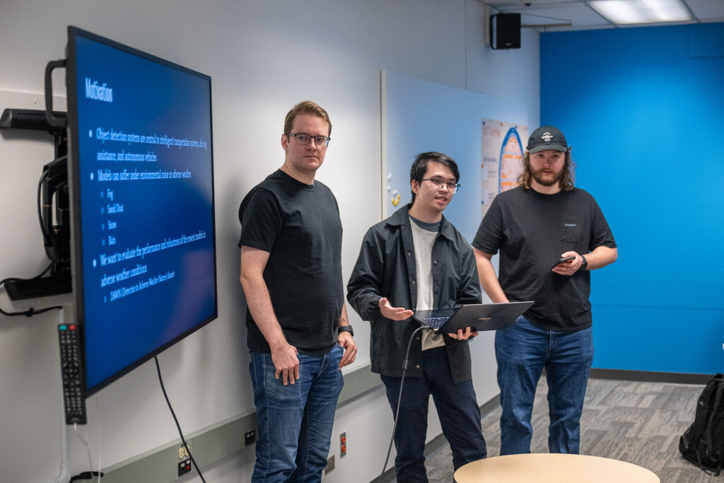 three students present data in a classroom