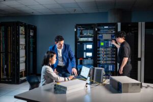Three people in a server room. Two people looking at a computer screen and one person at the server.