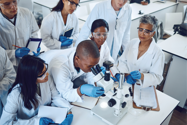 student looking through microscope with other students and instructor looking on