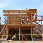 Participants working on a two-storey mass timber structure at BCIT campus, with a scissor lift and scaffolding visible alongside the glulam frame.