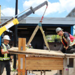 Participants using a knuckle boom crane to lift a glulam post, demonstrating rigging techniques at the BCIT mass timber practicum.