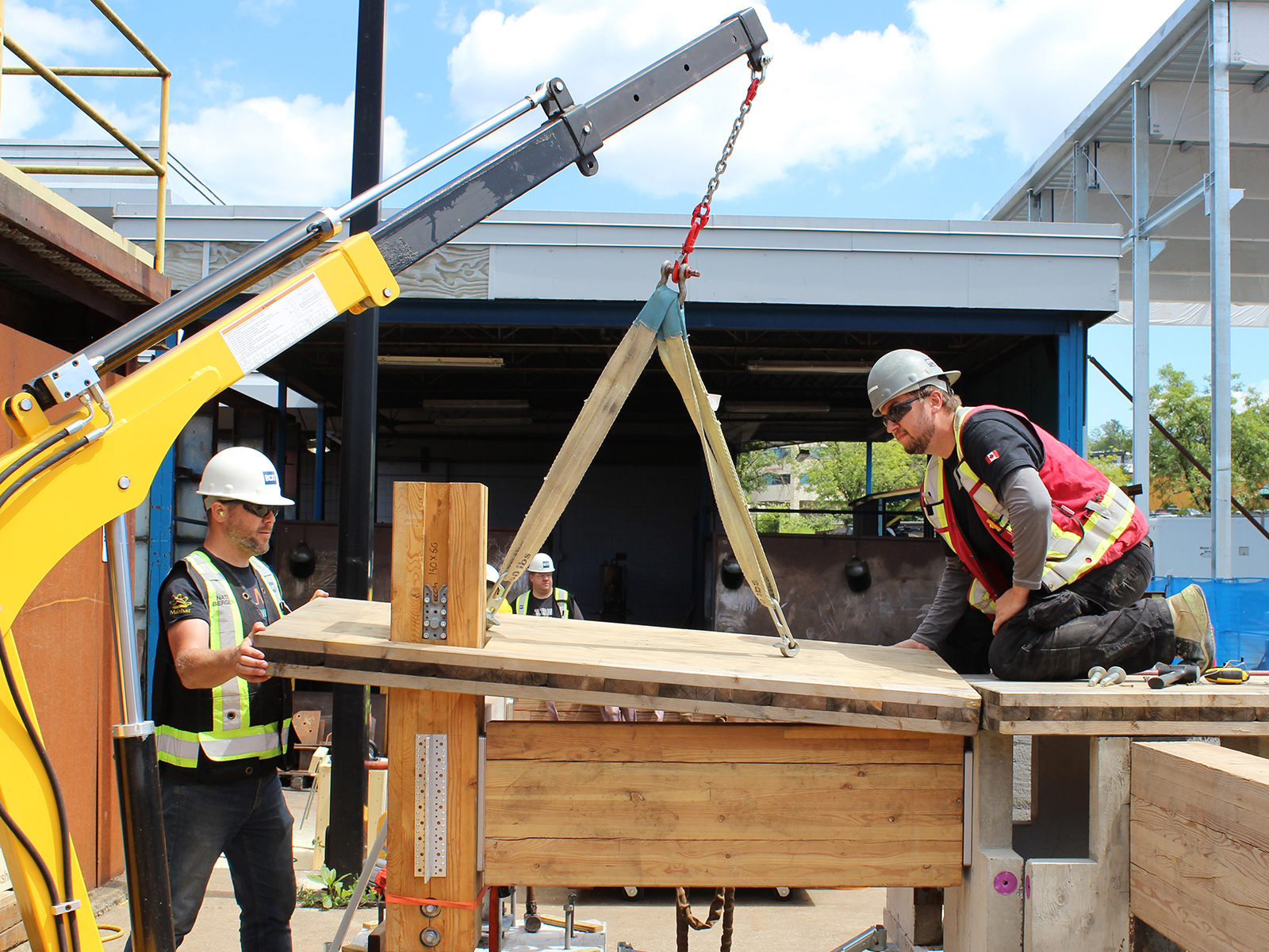 Participants using a knuckle boom crane to lift a glulam post, demonstrating rigging techniques at the BCIT mass timber practicum.