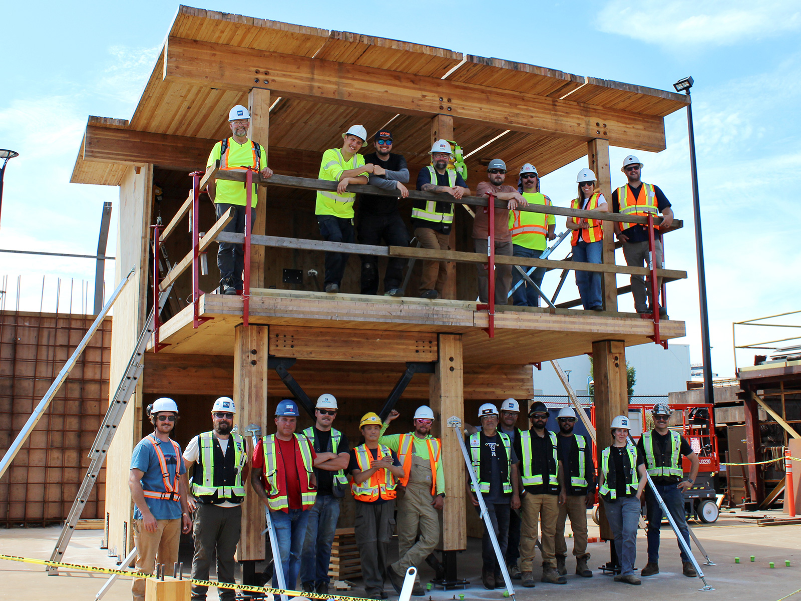 Group photo of practicum participants posing inside and on top of the completed two-storey mass timber structure at BCIT campus.